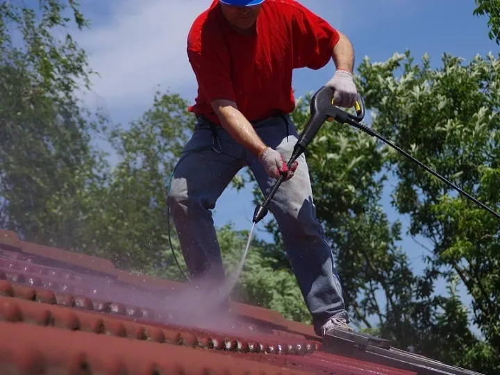 A man spraying a roof with a power washer.