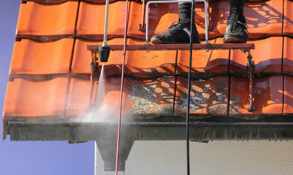 A man is spraying a roof with a pressure washer.