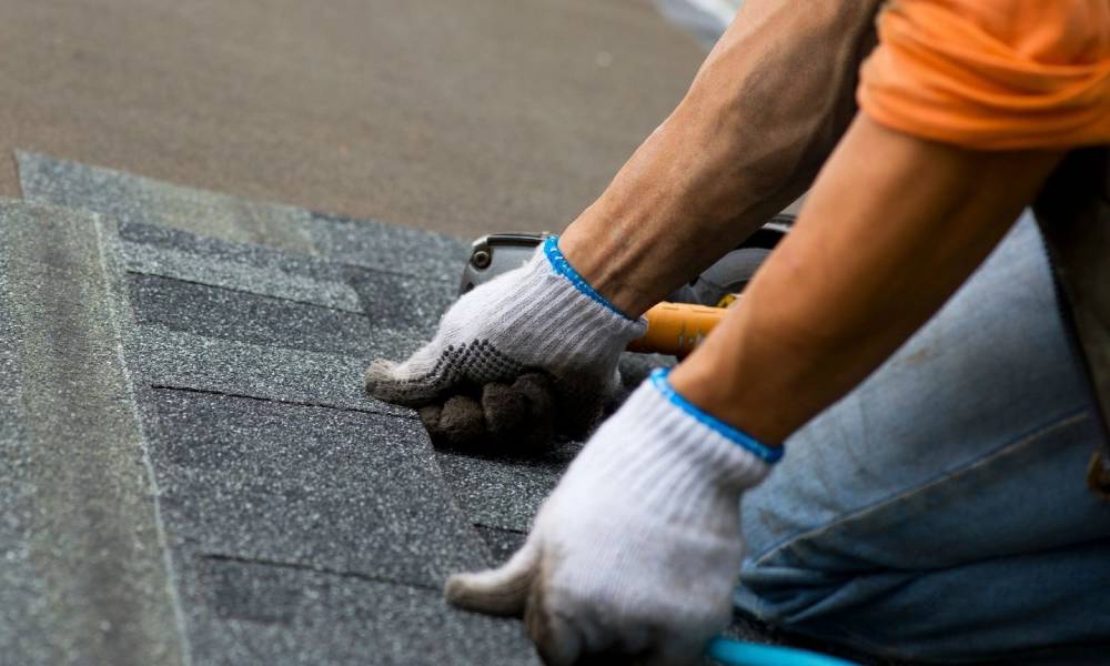 A man is working on a shingled roof.